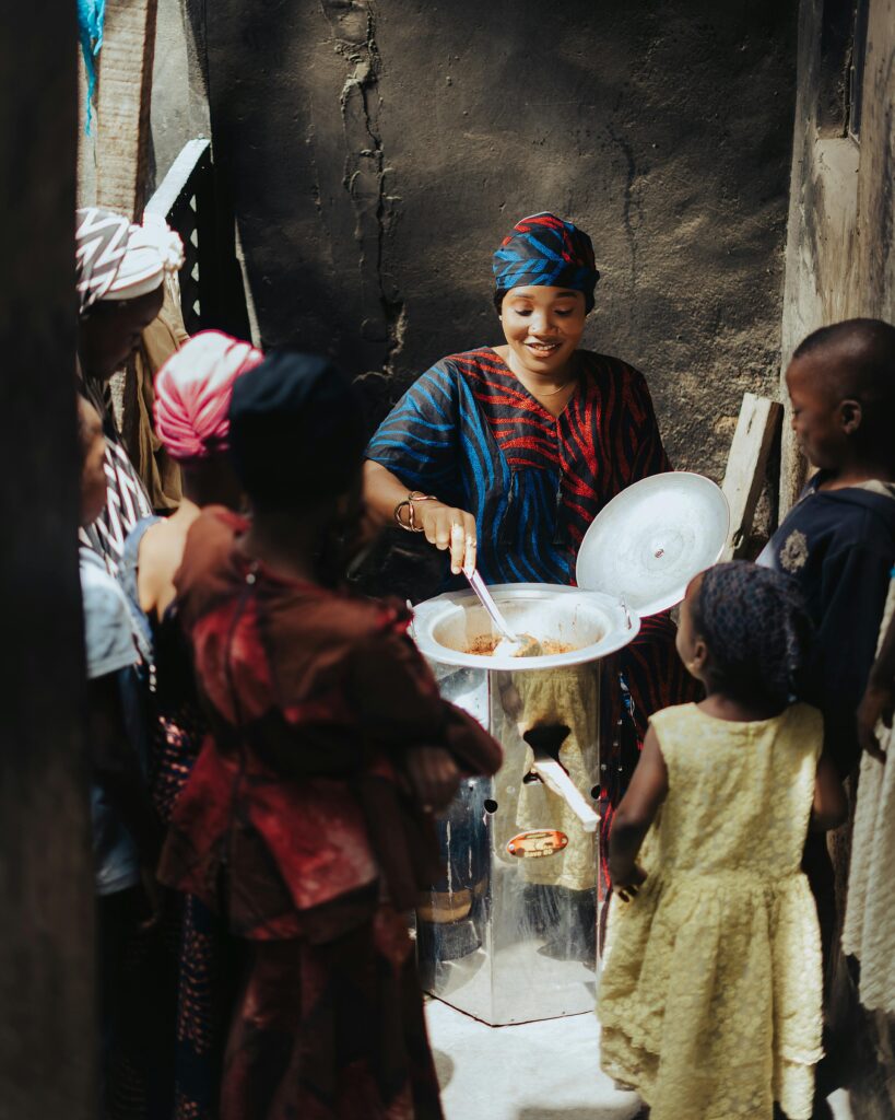 African woman cooking surrounded by cheerful children outdoors in a village setting.